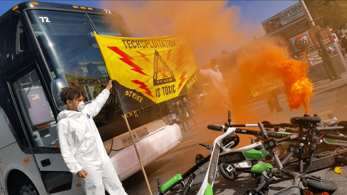 Photo of protesters in front of a tech shuttle with a pile of Lime scooters and a sign saying 'Techsploitation is toxic' Photo of protesters in front of a tech shuttle with a pile of Lime scooters and a sign saying 'Techsploitation is toxic'