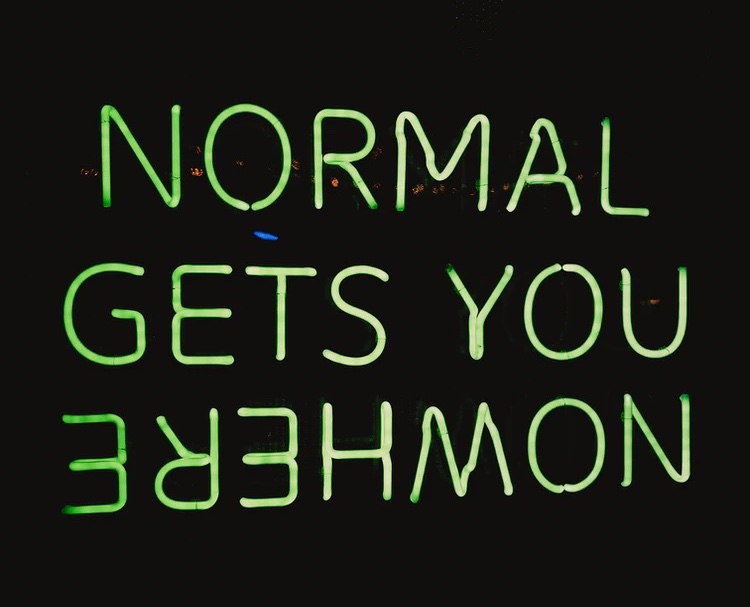A neon green sign on a black background that says NORMAL GETS YOU NOWHERE, with NOWHERE upside down and backwards A neon green sign on a black background that says NORMAL GETS YOU NOWHERE, with NOWHERE upside down and backwards
