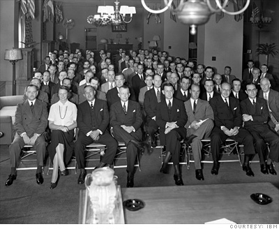 Black-and-white photograph showing a seated audience, most of whom are men wearing suits. Black-and-white photograph showing a seated audience, most of whom are men wearing suits.