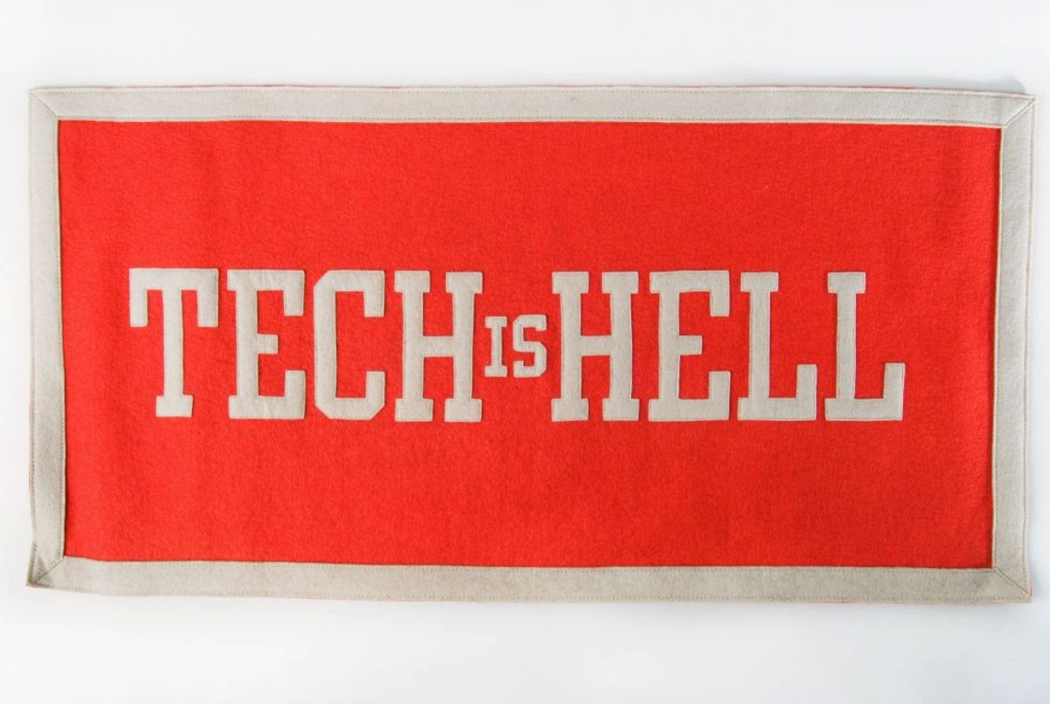 A red felt banner with white block letters that read Tech is Hell A red felt banner with white block letters that read Tech is Hell