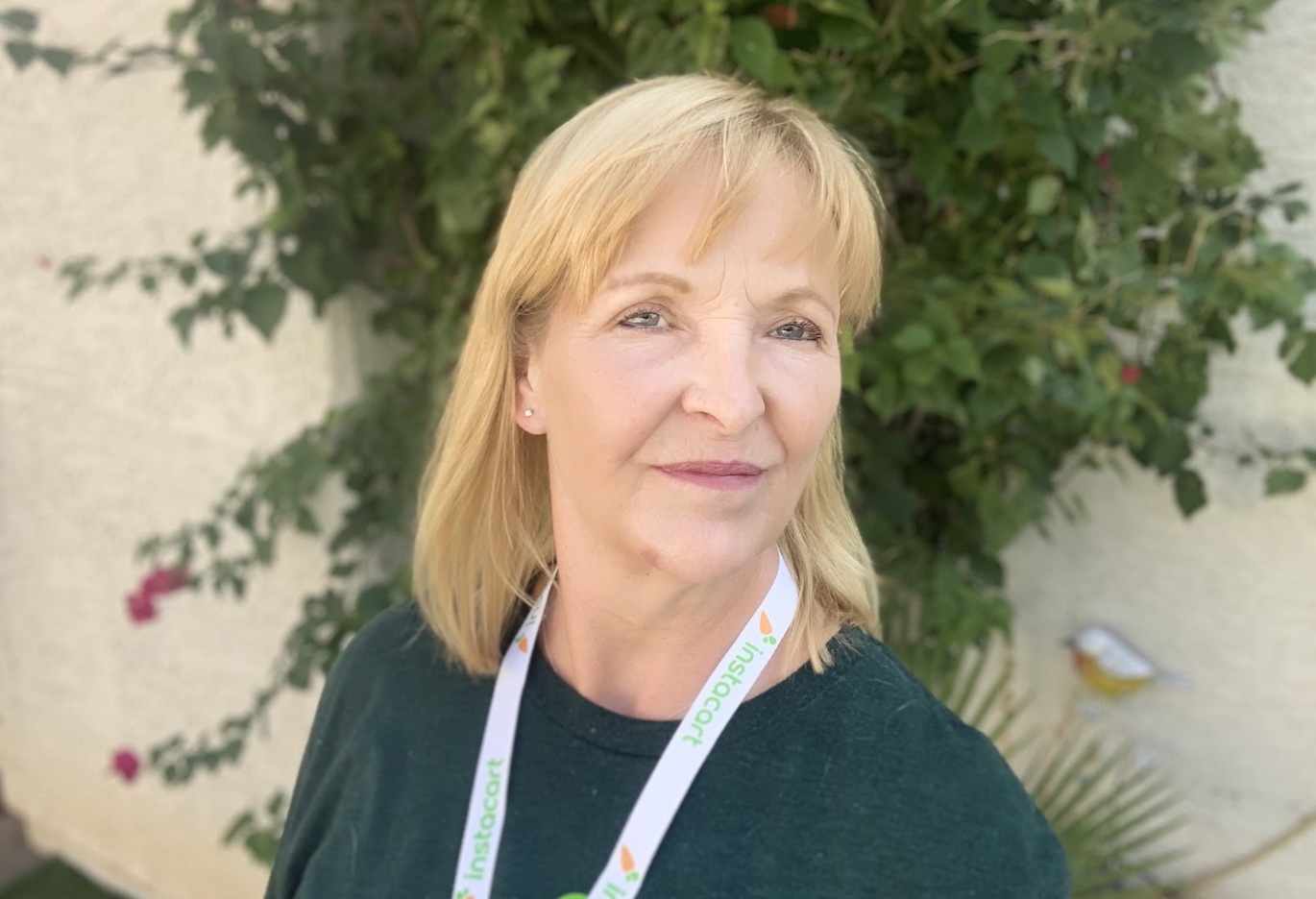 Photo of a blonde older and wiser woman wearing an Instacart lanyard in front of a wall with ivy Photo of a blonde older and wiser woman wearing an Instacart lanyard in front of a wall with ivy