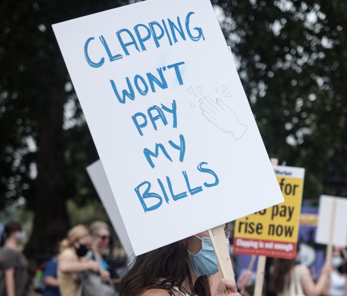 A person holding a sign that says CLAPPING WON'T PAY MY BILLS A person holding a sign that says CLAPPING WON'T PAY MY BILLS