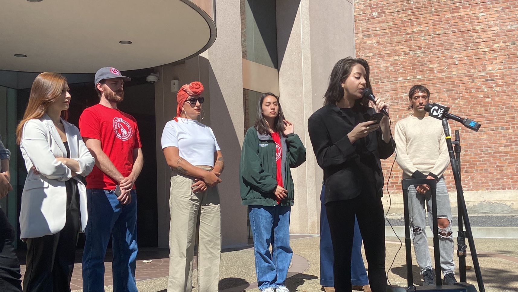 Eight Alphabet workers in casual clothing speaking on a mic in front of headquarters with a brick wall behind them Eight Alphabet workers in casual clothing speaking on a mic in front of headquarters with a brick wall behind them