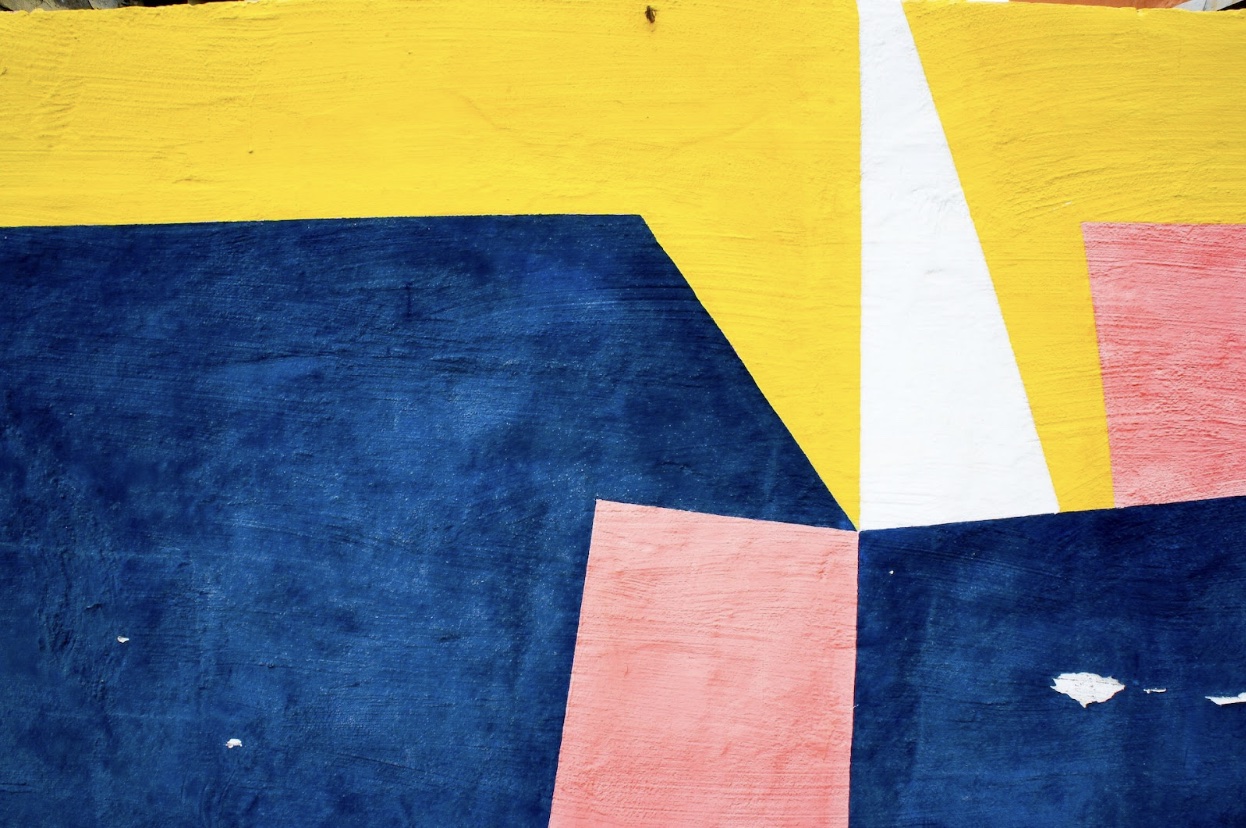 Seven painted abstract angular yellow pink and blue shapes of varying size, converging to the right of the middle of the canvas Seven painted abstract angular yellow pink and blue shapes of varying size, converging to the right of the middle of the canvas