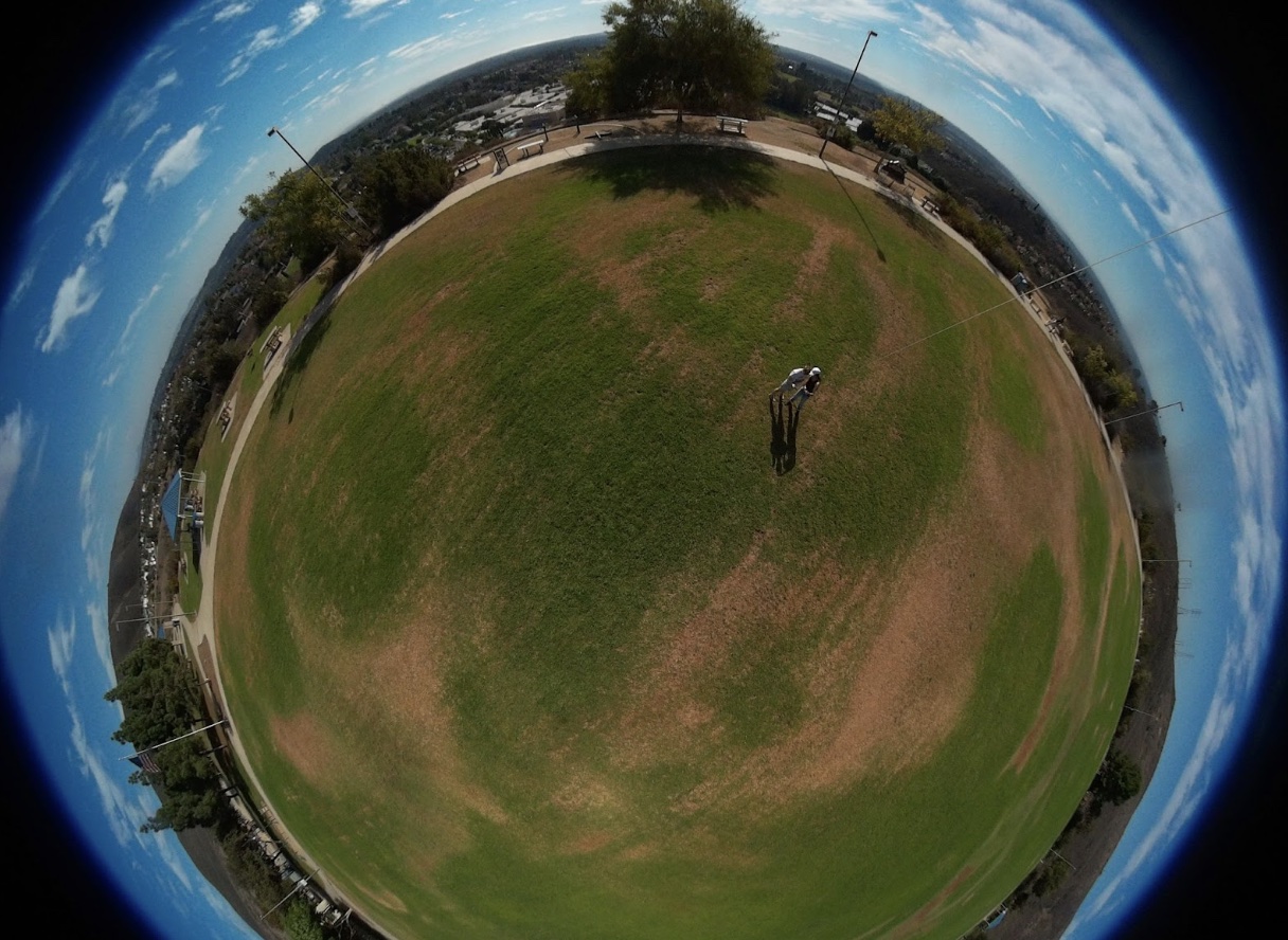 A fisheye lense photo of a large grassy sphere with two people standing A fisheye lense photo of a large grassy sphere with two people standing