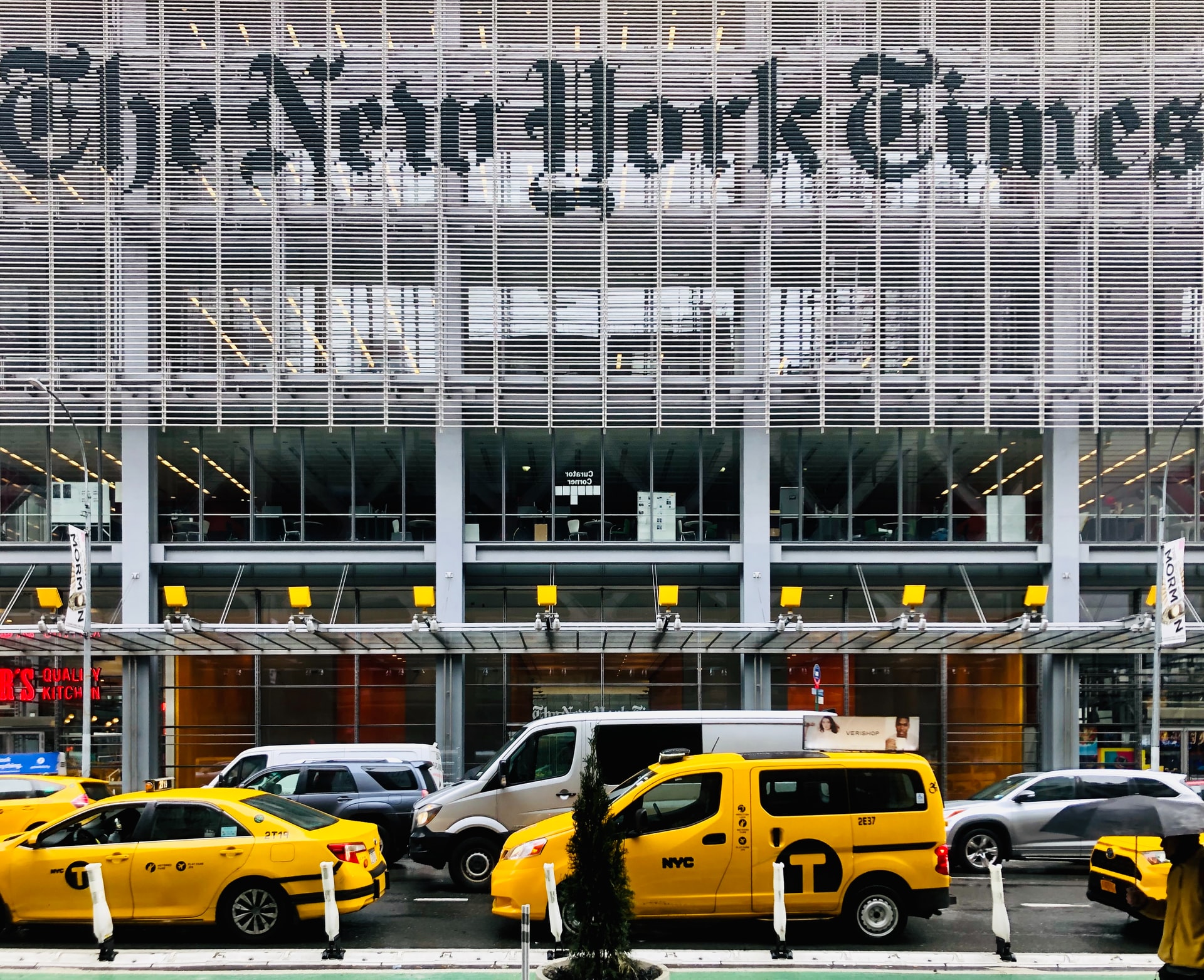 A view of facade of the New York Times Company, a grey metal and glass wall, with taxis and cars in front. A view of facade of the New York Times Company, a grey metal and glass wall, with taxis and cars in front.