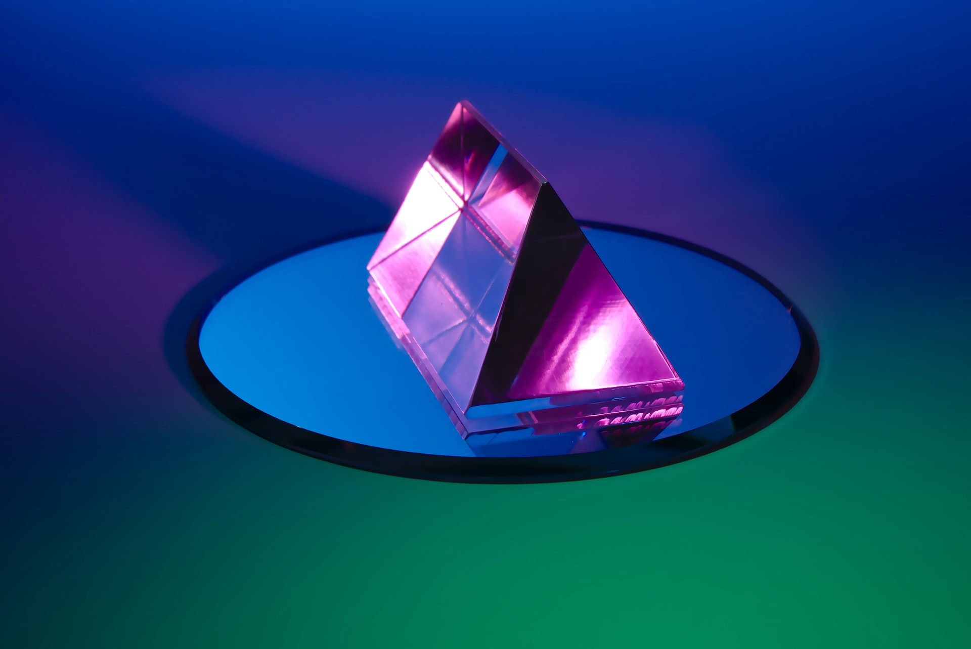 A neon pink prism on round blue mirror with a blue and green gradient background A neon pink prism on round blue mirror with a blue and green gradient background